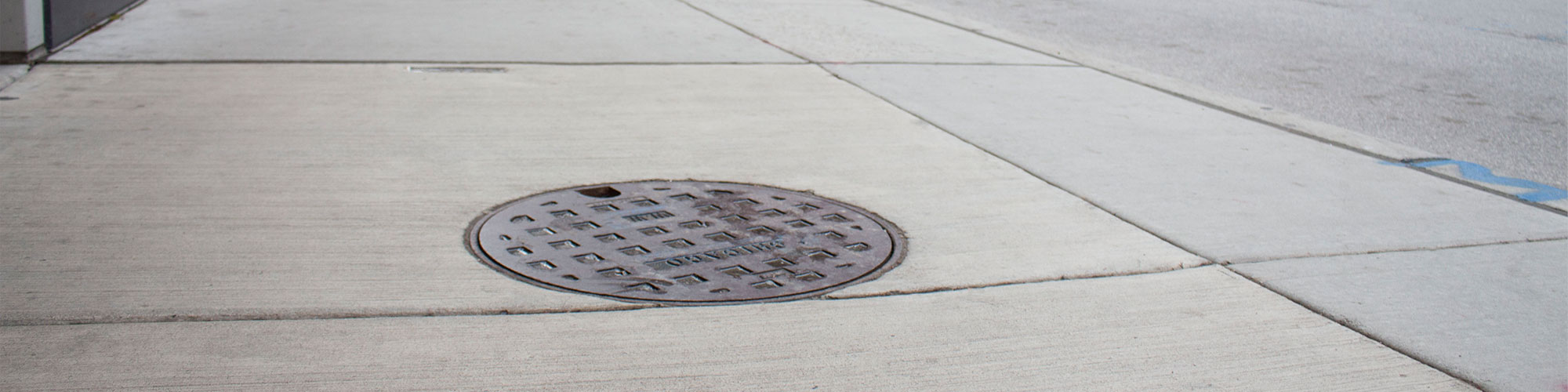 EJ manhole cover in sidewalk by city street with cars