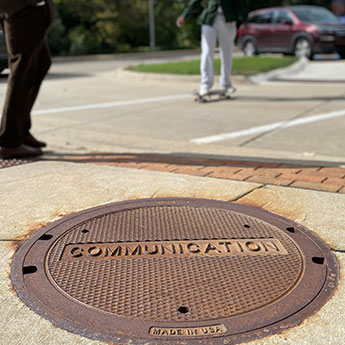 EJ communications telecommunication manhole cover in sidewalk with people walking by