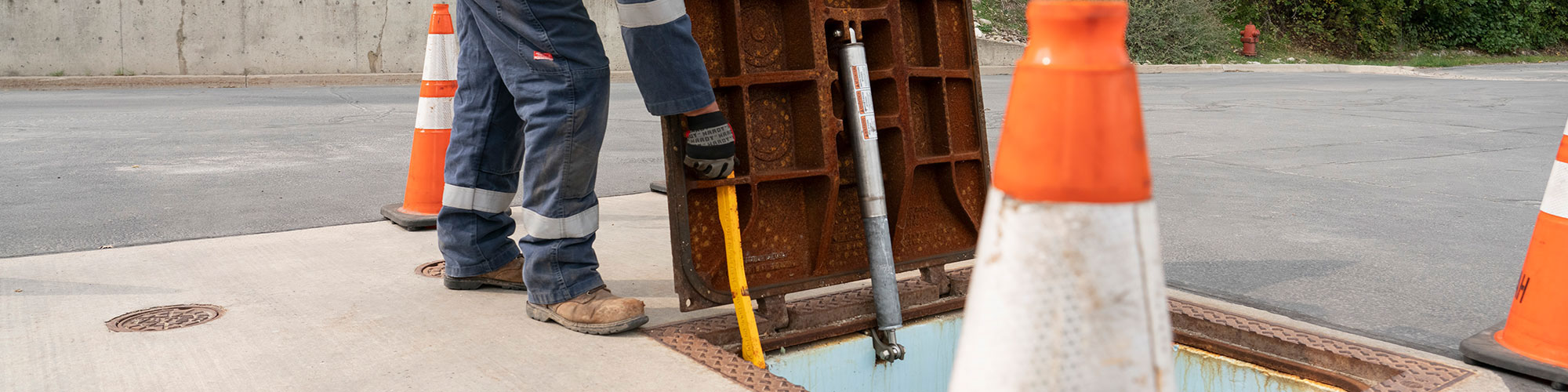 EJ ductile iron hatch with lift assist and safety bar being lifted by man in gloves